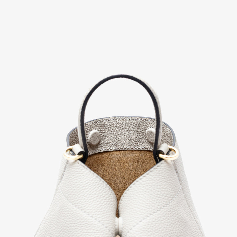 Close up of the top of Stow London's Mini Curve in Cloud Grey pebbled leather featuring the hidden magnets, suede lining and gold hardware on a light grey background 