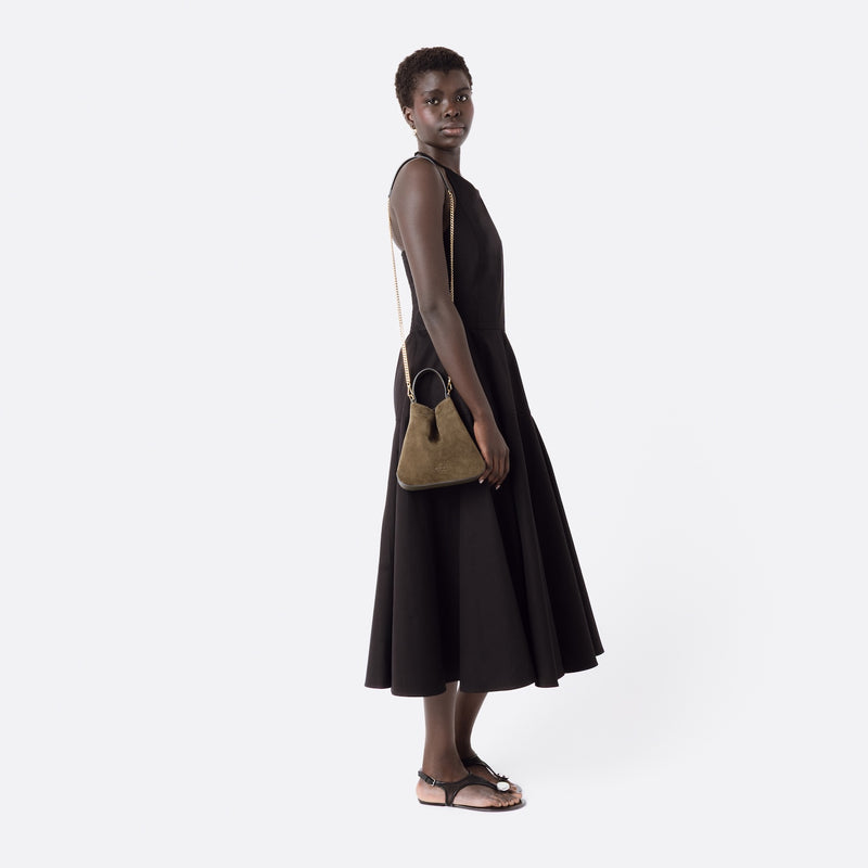 Model wearing Stow London's Mini Curve in Dark Green suede leather on her shoulder featuring gold-coated stainless steel hardware on a light grey background 