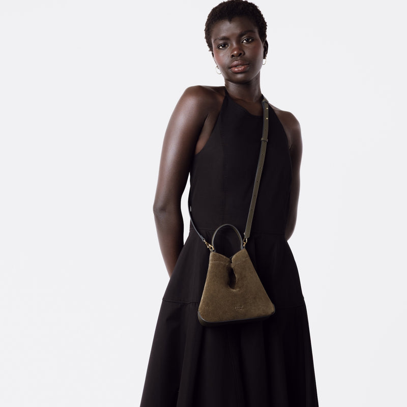 Model wearing STOW London's Mini Curve in Dark Green suede leather with the detachable leather crossbody strap on a white background 