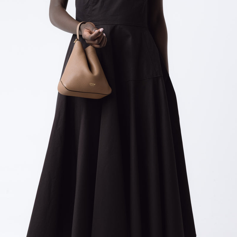 Model holding STOW London's Mini Curve in Mocha pebbled leather on her wrist on a white background