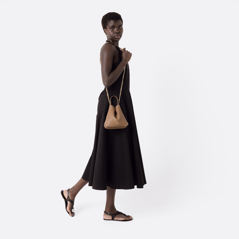 Model wearing STOW London's Mini Curve in Mocha leather on her shoulder featuring by gold-plated chain on a white background