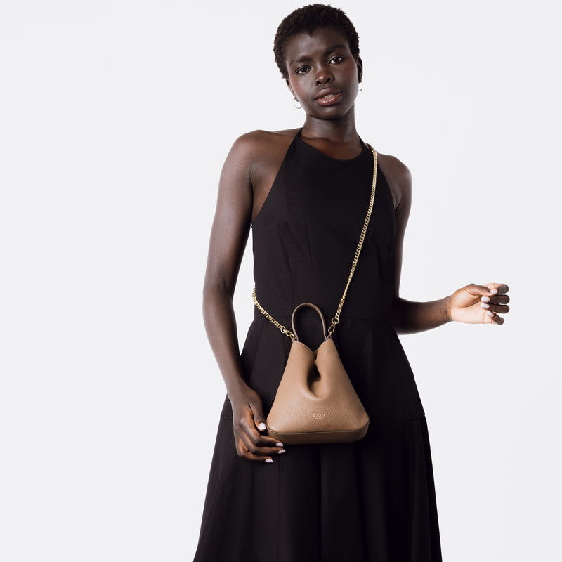 Model wearing STOW London's Mini Curve in Mocha leather crossbody with gold-plated chain on a white background