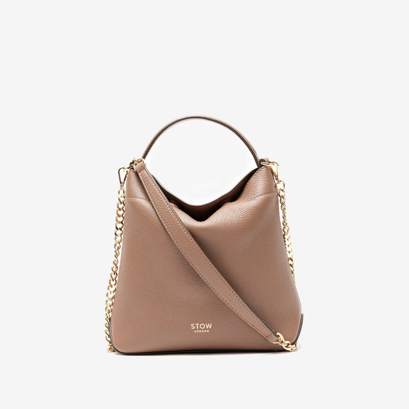 Stow London's Mini Curve in Mocha pebbled leather and detachable gold chain crossbody strap styled as a flap bag on a light grey background 