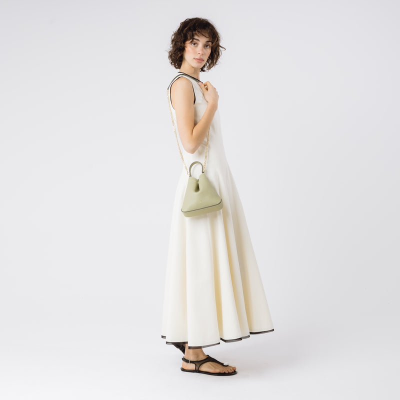 Model wearing STOW London's Mini Curve in Pale Green pebbled leather on he shoulder by detachable gold chain crossbody strap on a white background 