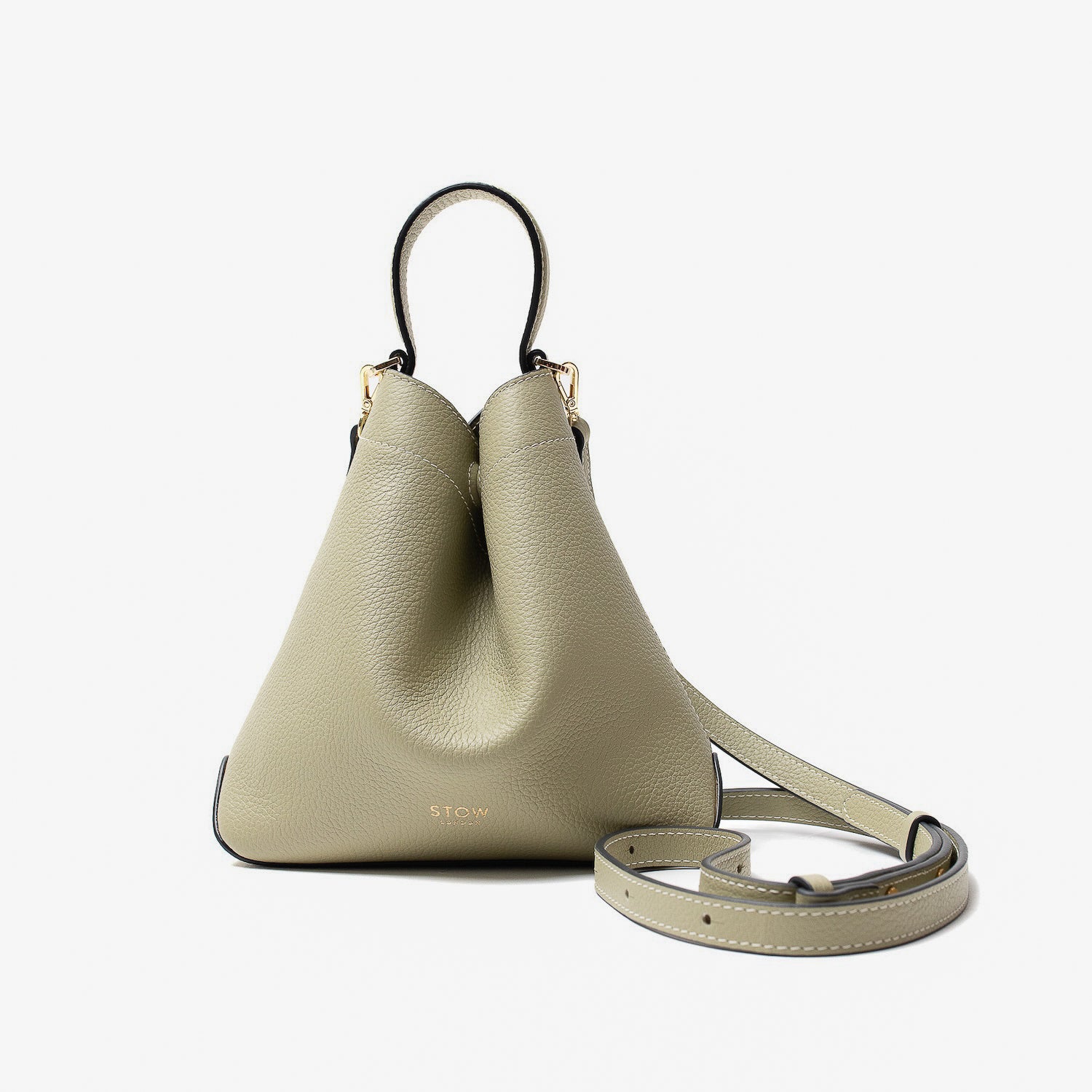 STOW London's Mini Curve in Pale Green pebbled leather and detachable leather crossbody strap on a light grey background 