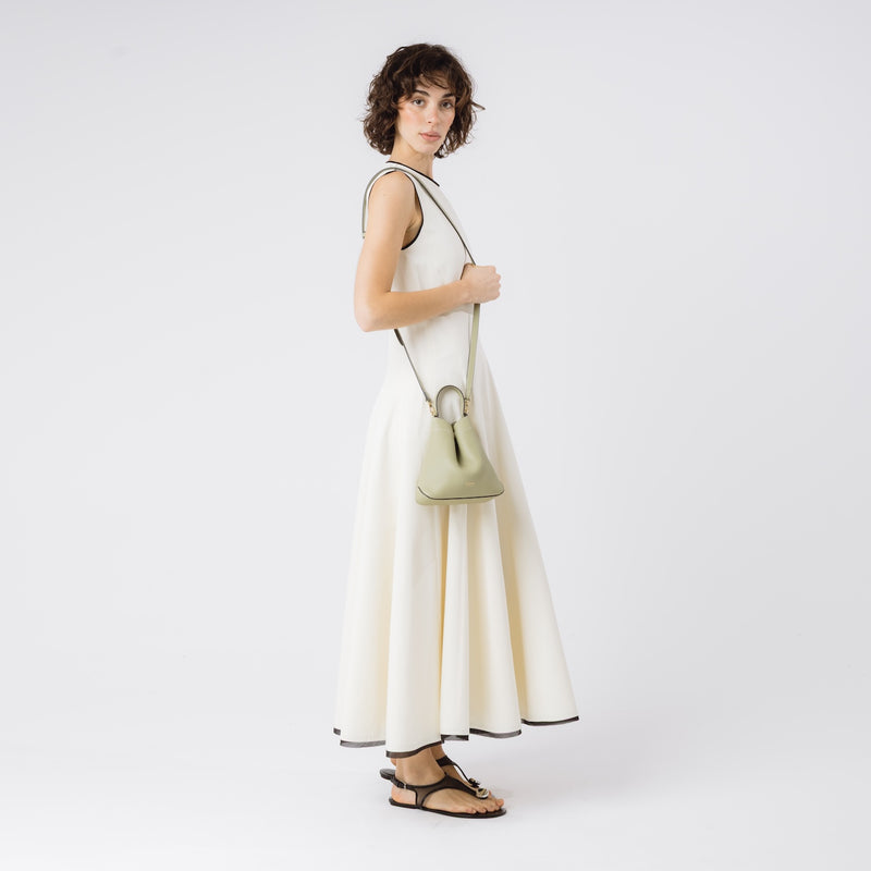 Model wearing STOW London's Mini Curve in Pale Green pebbled leather with the detachable leather crossbody strap on her shoulder on a white background 