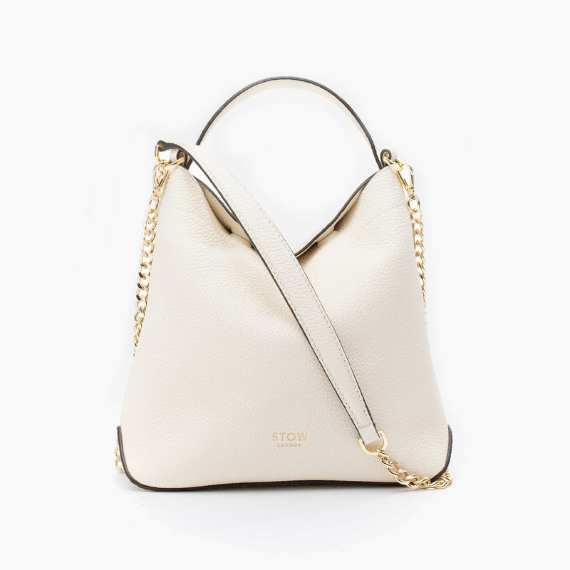 STOW London's Mini Curve in Spring Moon pebbled leather and detachable gold chain crossbody strap styled as a flap bag on a light grey background 