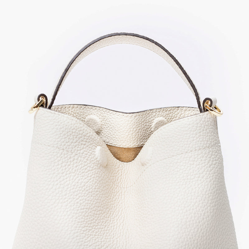 Close up of STOW London's Mini Curve in Spring Moon pebbled leather featuring hidden magnets, suede lining and gold hardware on a light grey background 