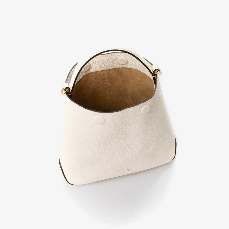 Top view of STOW London's Mini Curve in Spring Moon pebbled leather with magnets open showing cognac suede interior lining on a light grey background 