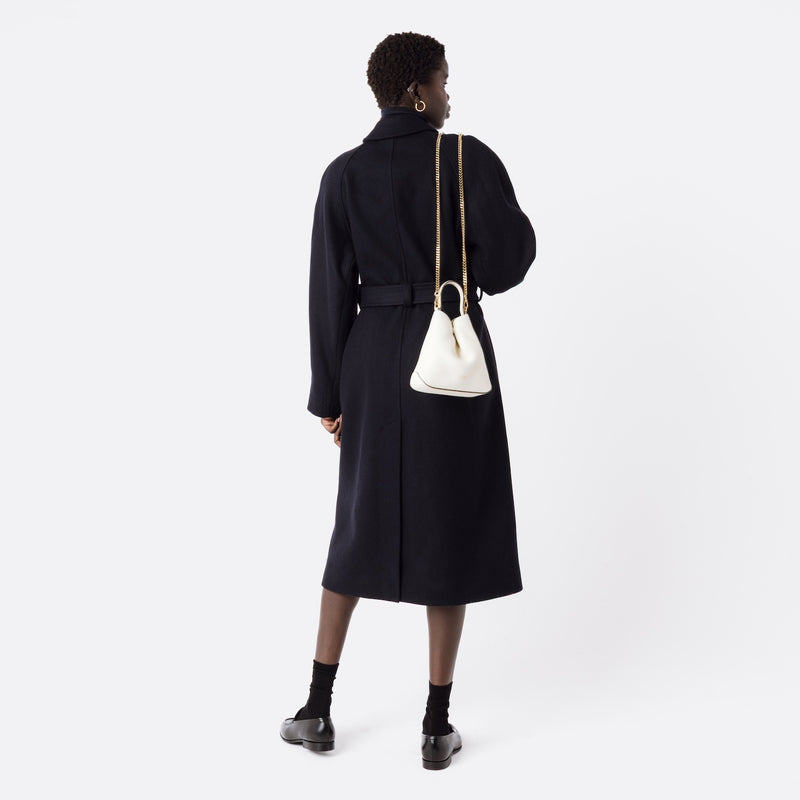 Model holding STOW London's Mini Curve in Spring Moon pebbled leather over her shoulder with the gold-plated chain strap on a white background 