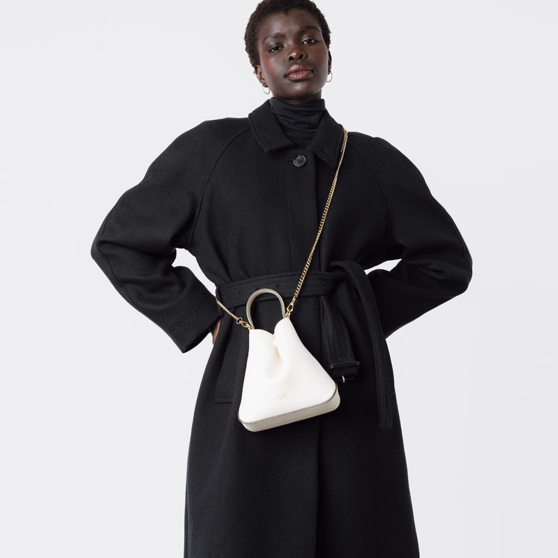 Model wearing STOW London's Mini Curve in Spring Moon pebbled leather crossbody by gold chain strap on a white background 