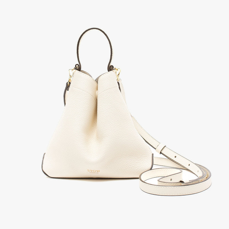STOW London's Mini Curve in Spring Moon pebbled leather and detachable leather crossbody strap on a light grey background 