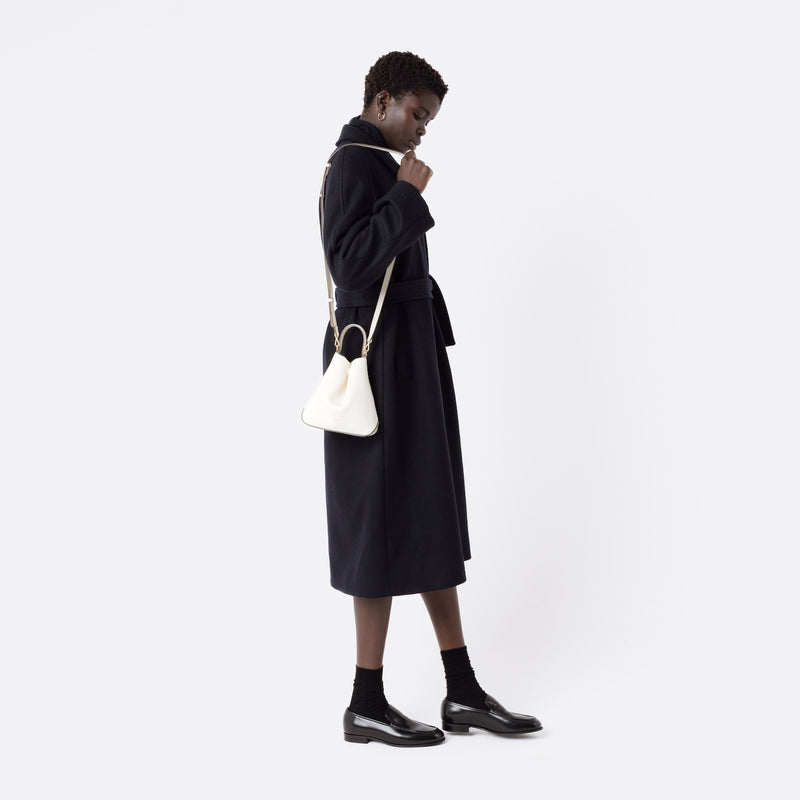 Model wearing STOW London's Mini Curve in Spring Moon pebbled leather with the detachable leather crossbody strap on her shoulder on a white background 