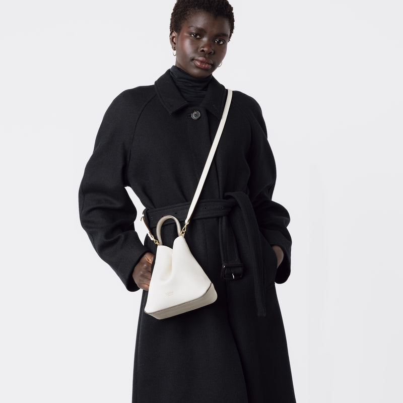 Model wearing STOW London's Mini Curve in Spring Moon pebbled leather with the detachable leather crossbody strap on a white background 