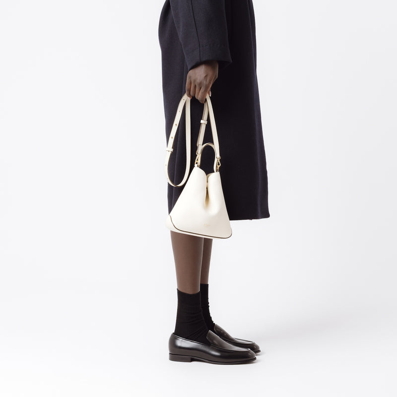 Model holding STOW London's Mini Curve in Spring Moon pebbled leather by the detachable leather crossbody strap on a white background 