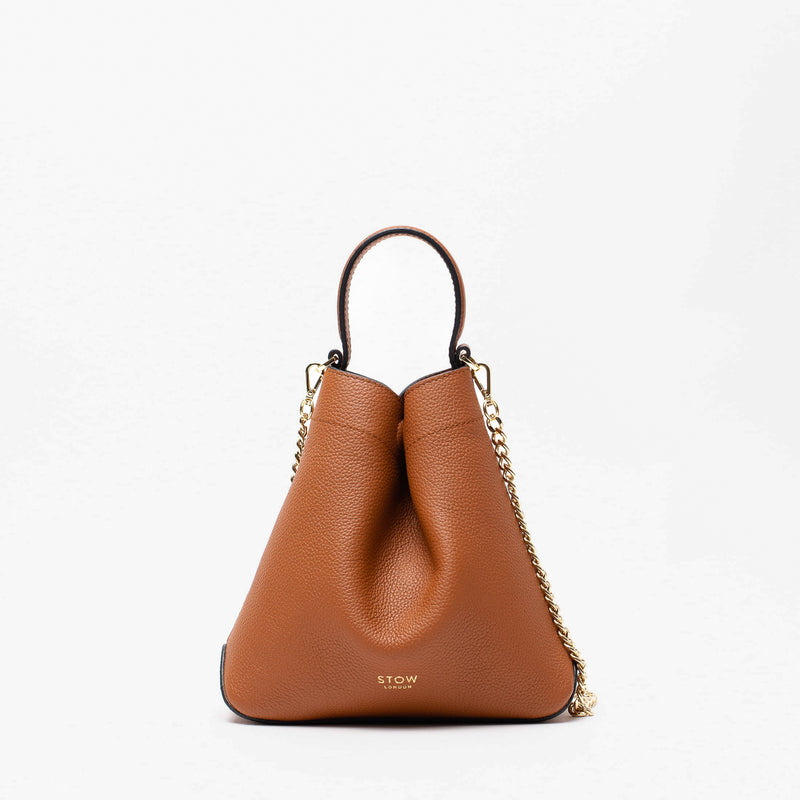 Stow London's Mini Curve in Earth tan pebbled leather and detachable gold chain crossbody strap on a light grey background 