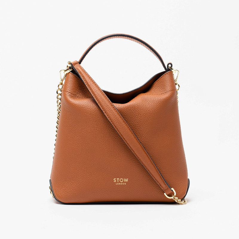 Stow London's Mini Curve in Earth tan pebbled leather and detachable gold chain crossbody strap styled as a flap bag on a light grey background 
