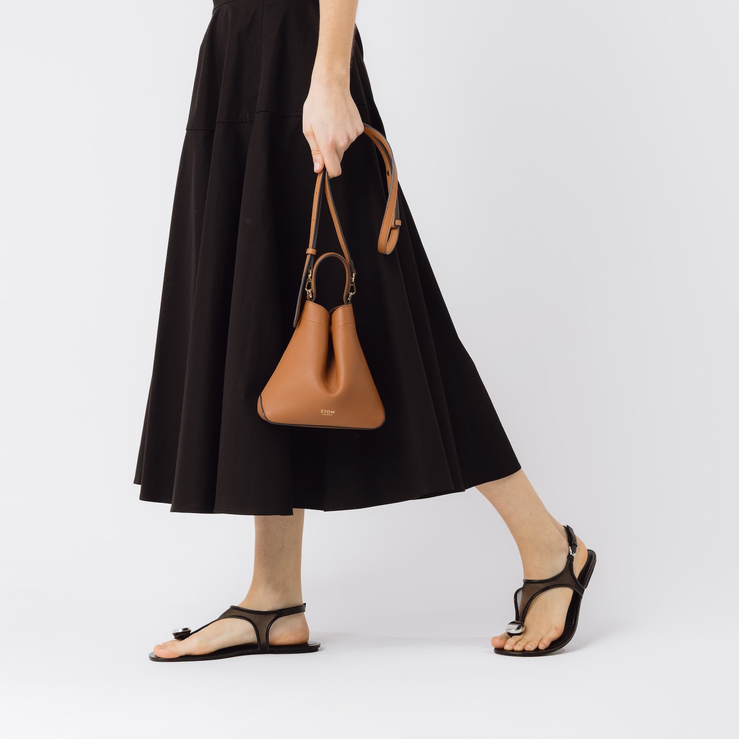 STOW London's Mini Curve in Earth Tan held by model by detachable leather strap featuring gold-coated stainless steel hardware on a white background