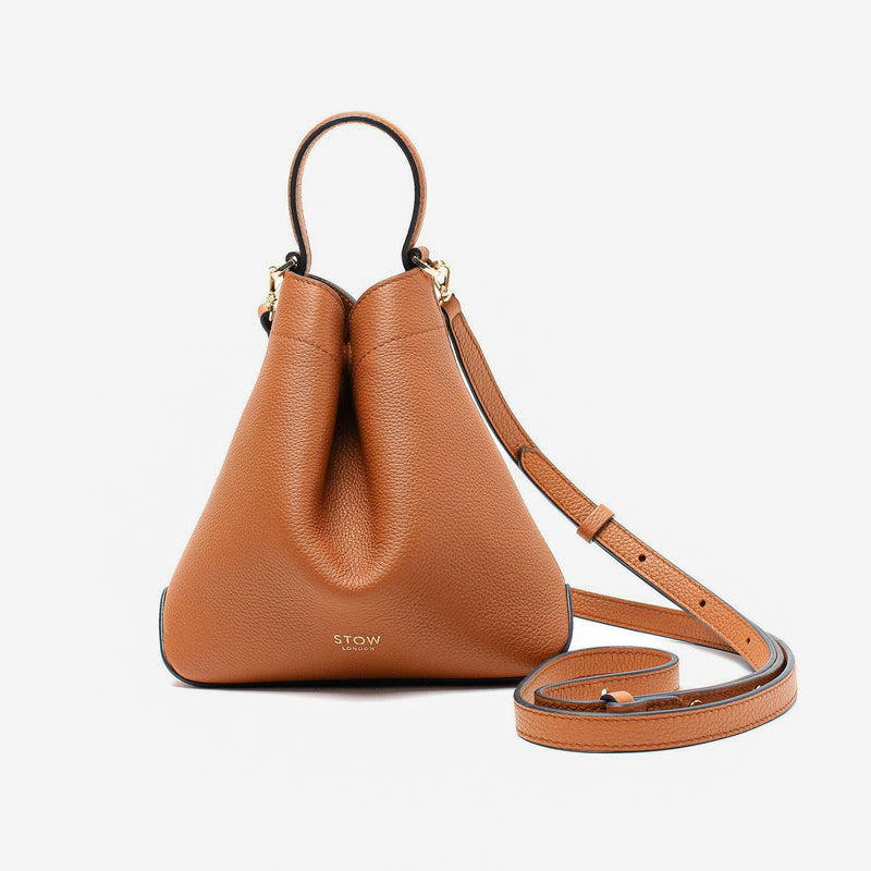 STOW London's Mini Curve in Earth Tan pebbled leather and detachable leather crossbody strap on a light grey background 