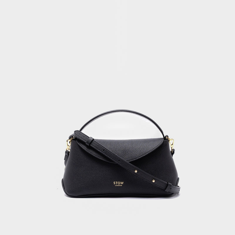 STOW London's Mini East West in Black pebbled leather and detachable crossbody strap featuring gold-coated stainless steel hardware on a light grey background