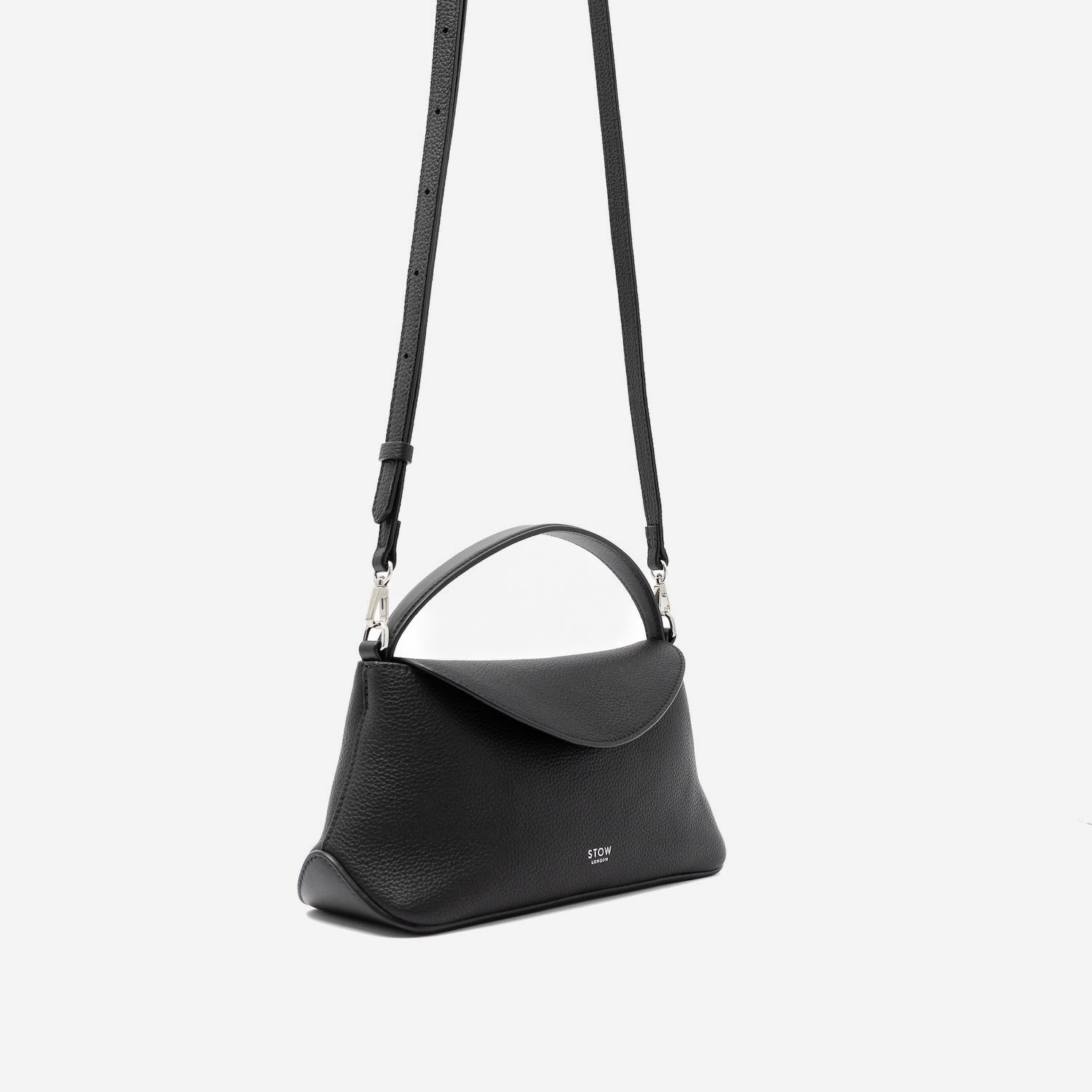 Off-axis view of STOW London's Mini East West in Black pebbled leather and detachable crossbody strap featuring silver stainless steel hardware on a light grey background