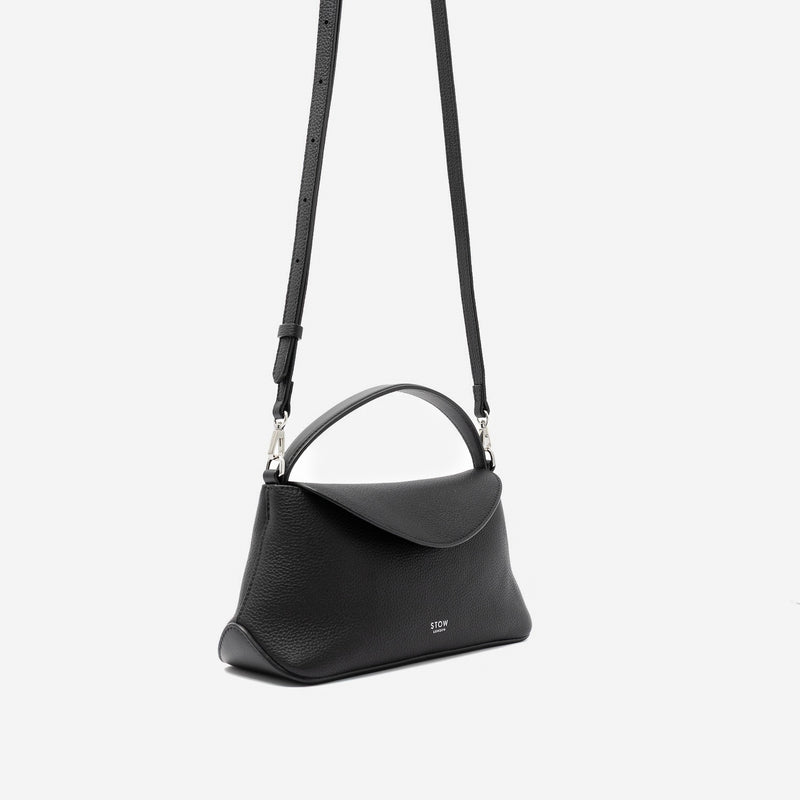 Off-axis view of STOW London's Mini East West in Black pebbled leather and detachable crossbody strap featuring silver stainless steel hardware on a light grey background