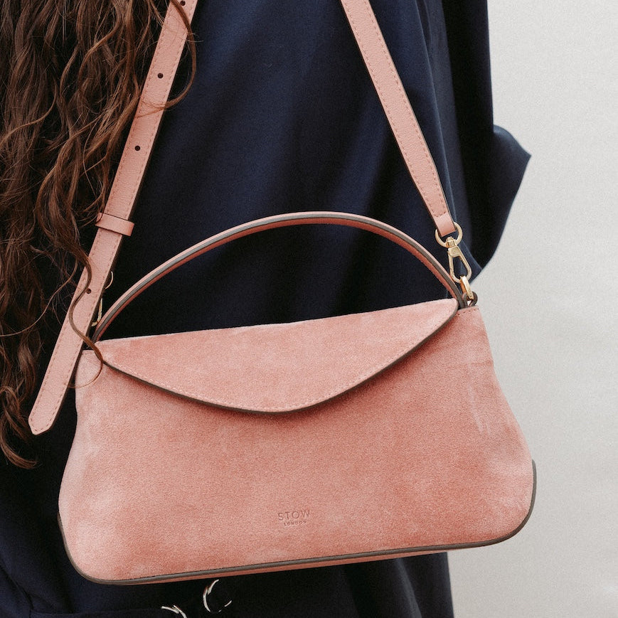 Model holding STOW London's Mini East West in Hazy Blush suede leather featuring gold-coated stainless steel hardware and its detachable crossbody strap