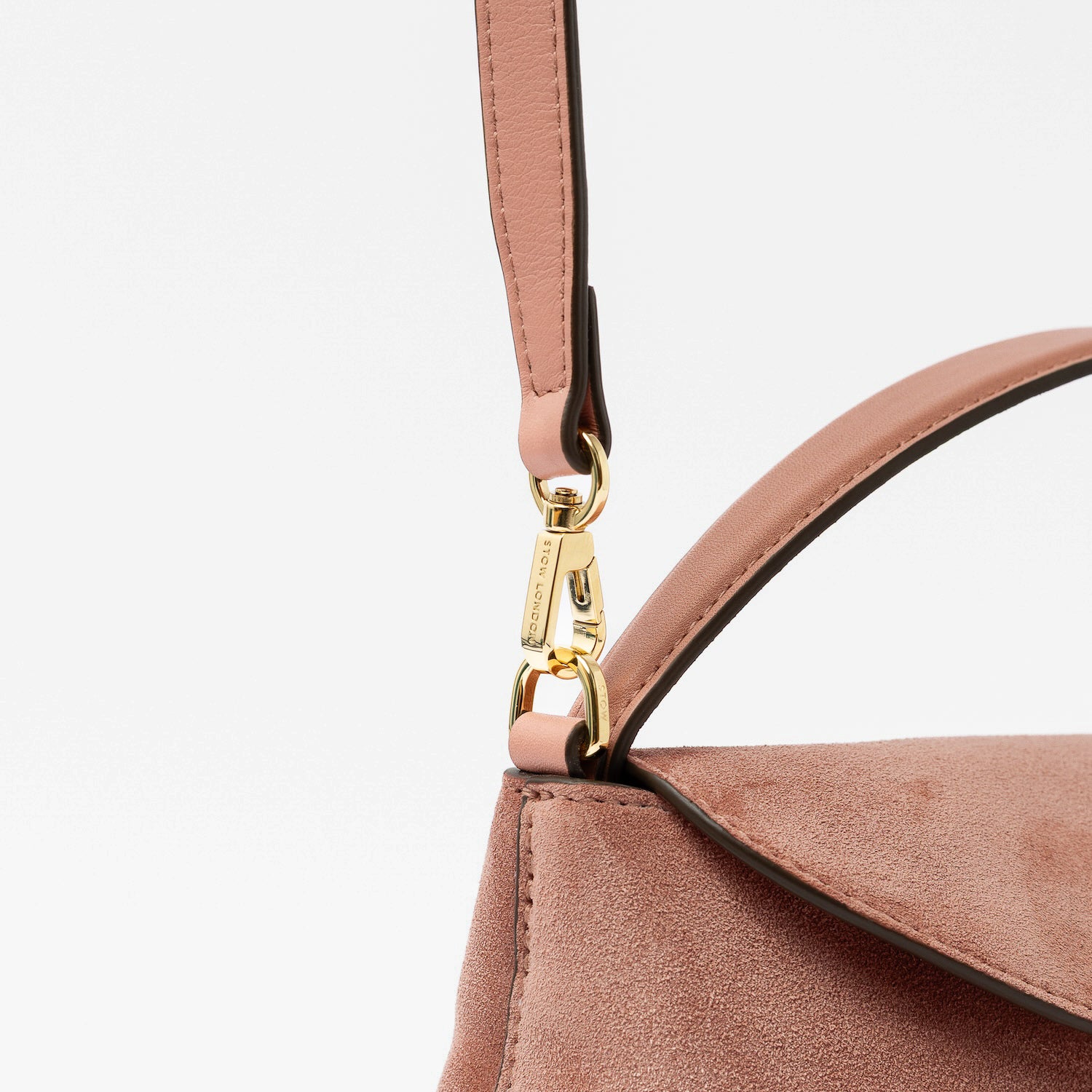 Close up of the detachable crossbody strap clip of STOW London's Mini East West in Hazy Blush suede leather featuring gold-coated stainless steel hardware on a light grey background