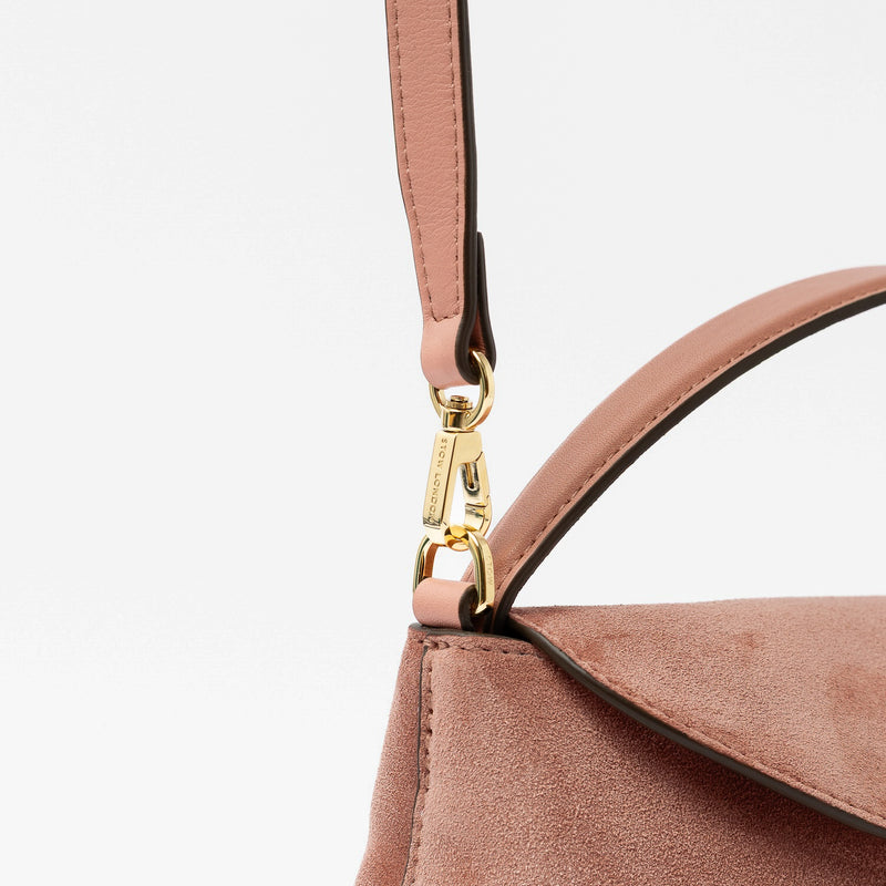 Close up of the detachable crossbody strap clip of STOW London's Mini East West in Hazy Blush suede leather featuring gold-coated stainless steel hardware on a light grey background