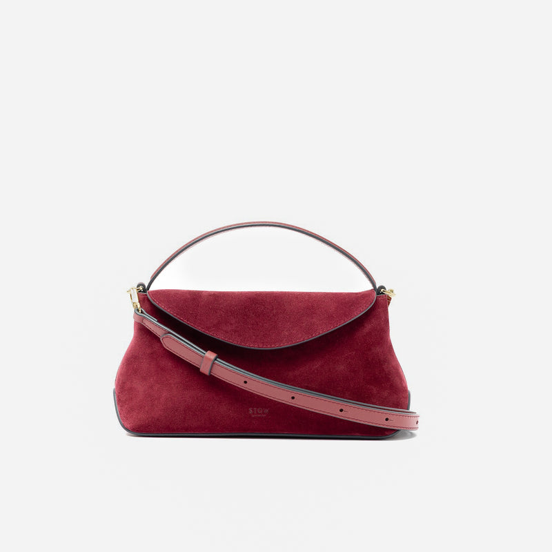 STOW London's Mini East West in Burgundy suede leather and detachable crossbody strap featuring gold-coated stainless steel hardware on a light grey background