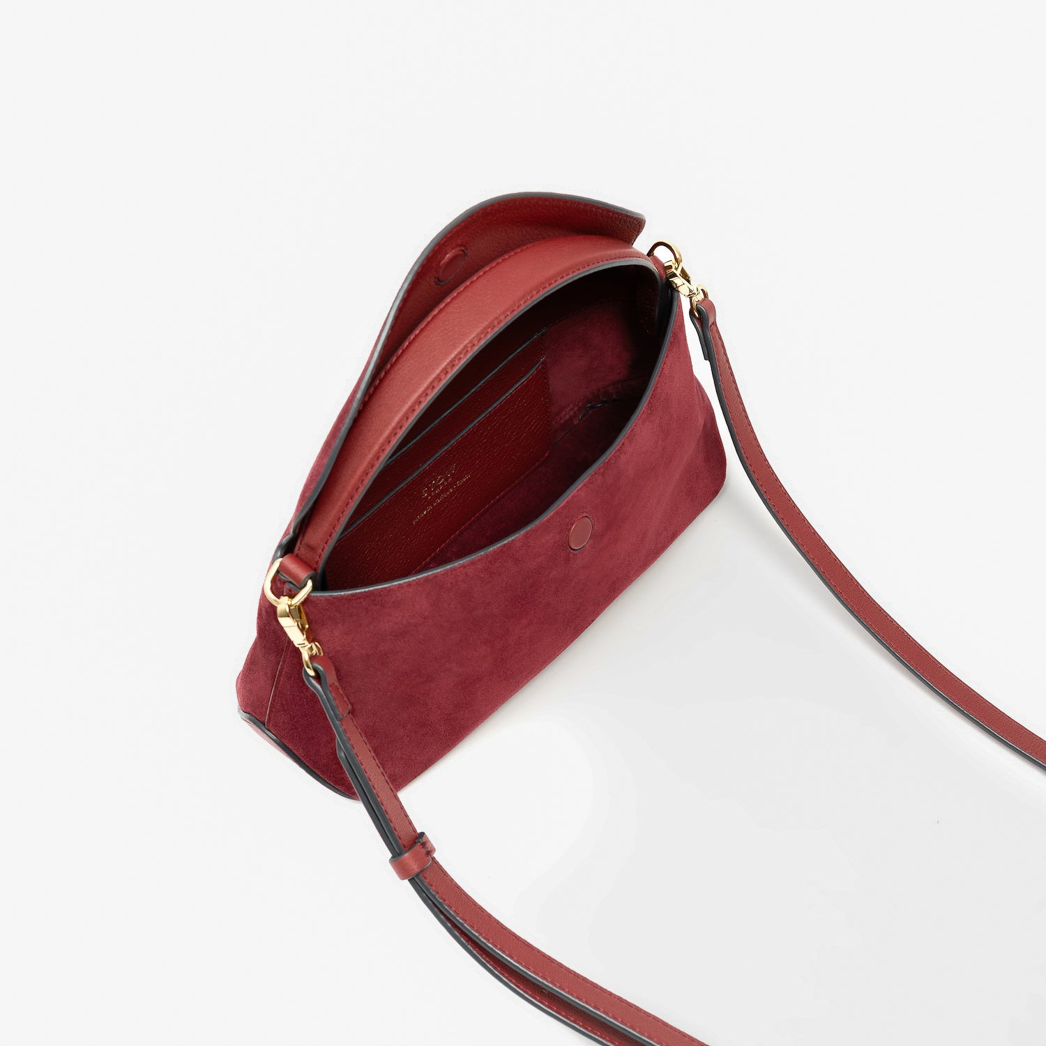 STOW London's Mini East West in Burgundy suede leather with flap open showing suede interior and slip pocket featuring gold-coated stainless steel hardware on a light grey background