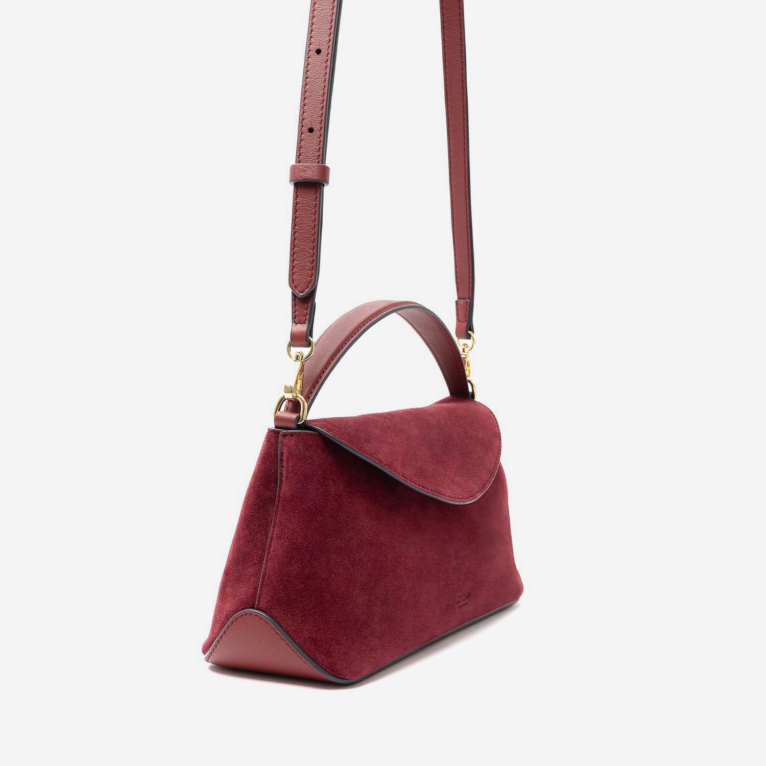 Off-axis view of STOW London's Mini East West in Burgundy suede leather and detachable crossbody strap featuring gold-coated stainless steel hardware on a light grey background