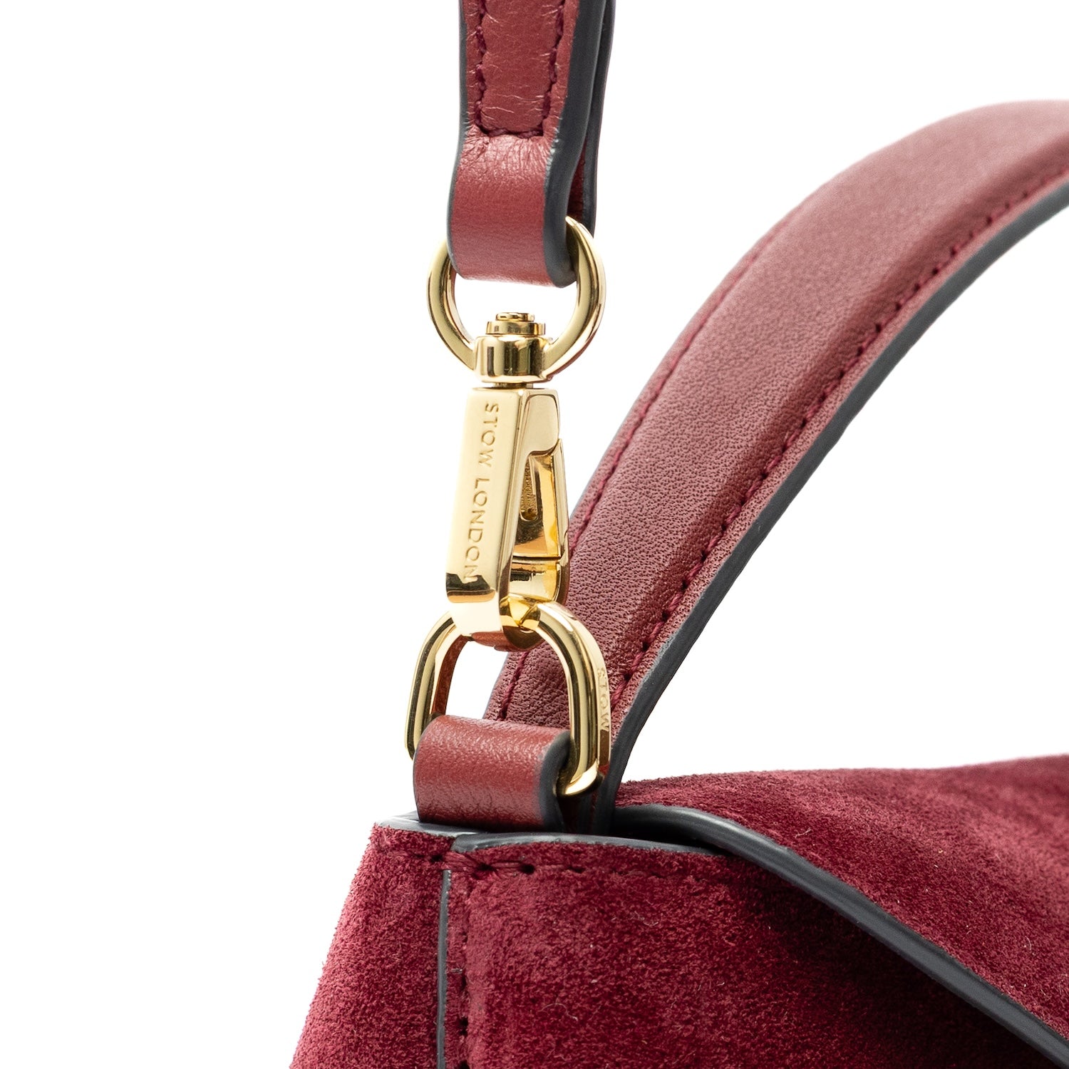 Close up of detachable clip of the detachable crossbody strap on STOW London's Mini East West bag in Burgundy Suede leather featuring gold-coated stainless steel hardware on a white background