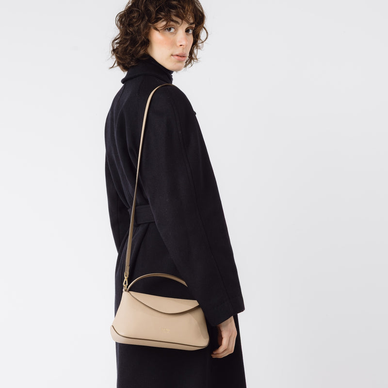 Model wearing STOW London's Mini East West in Camel leather on her shoulder featuring gold-coated stainless steel hardware on a white background