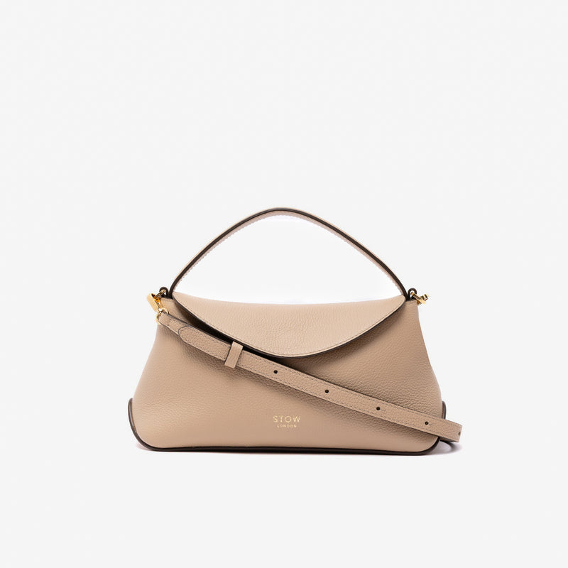 STOW London's Mini East West in Camel pebbled leather and detachable crossbody strap featuring gold-coated stainless steel hardware on a light grey background