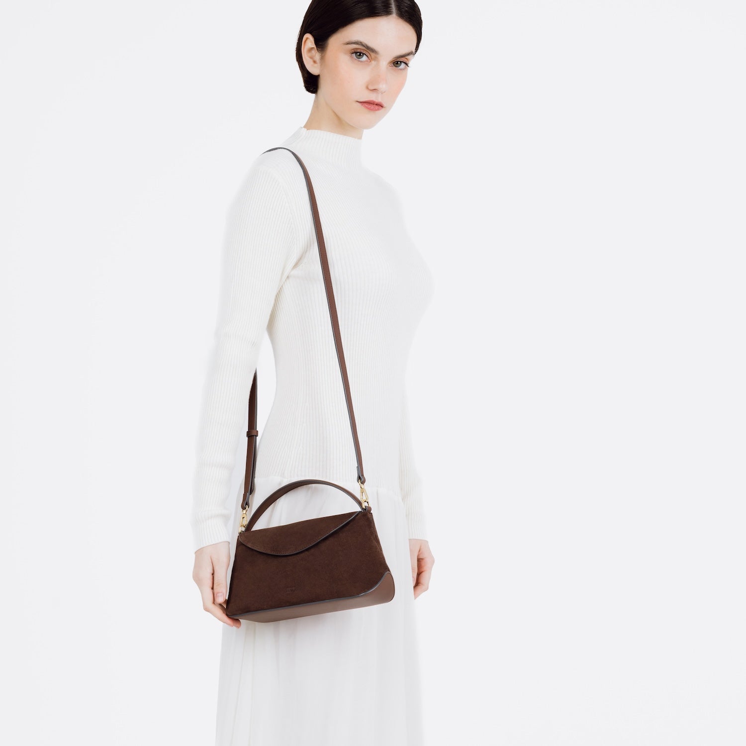 Model wearing STOW London's Mini East West bag in Chocolate Suede leather on her shoulder featuring gold-coated stainless steel hardware on a white background