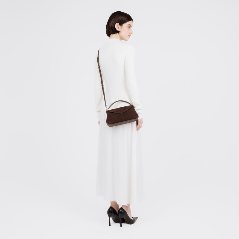 Model wearing STOW London's Mini East West bag in Chocolate Suede leather crossbody featuring gold-coated stainless steel hardware on a white background