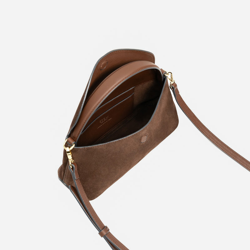 STOW London's Mini East West in Chocolate suede leather with flap open showing suede interior and slip pocket featuring gold-coated stainless steel hardware on a light grey background