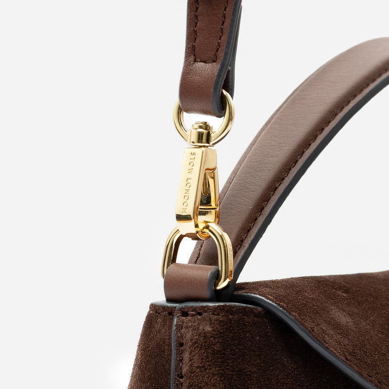 Close up of the detachable crossbody strap clip of STOW London's Mini East West in Chocolate suede leather featuring gold-coated stainless steel hardware on a light grey background