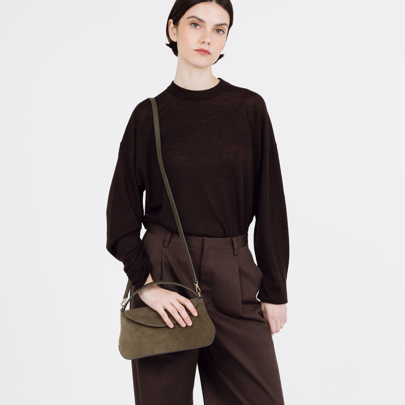 Model wearing STOW London's Mini East West bag in Dark Green Suede leather on her shoulder featuring gold-coated stainless steel hardware on a white background