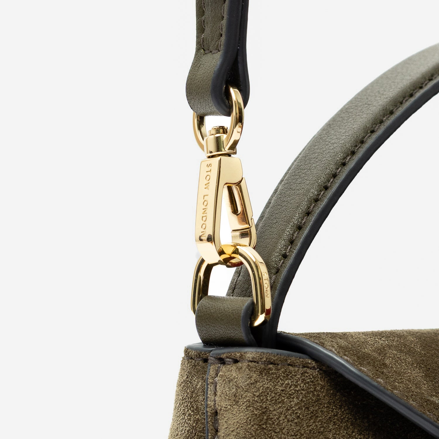 Close up of the detachable crossbody strap clip of STOW London's Mini East West in Dark Green suede leather featuring gold-coated stainless steel hardware on a light grey background