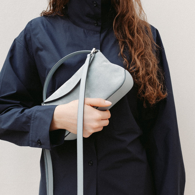 Model holding STOW London's Mini East West in Misty Blue suede leather featuring silver stainless steel hardware and its detachable crossbody strap