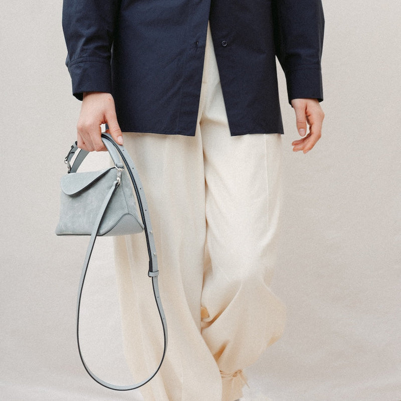 Model holding STOW London's Mini East West in Misty Blue suede leather at her side featuring silver stainless steel hardware and its detachable crossbody strap