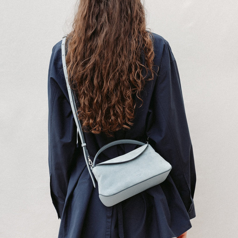 Model wearing STOW London's Mini East West in Misty Blue suede leather crossbody featuring silver stainless steel hardware