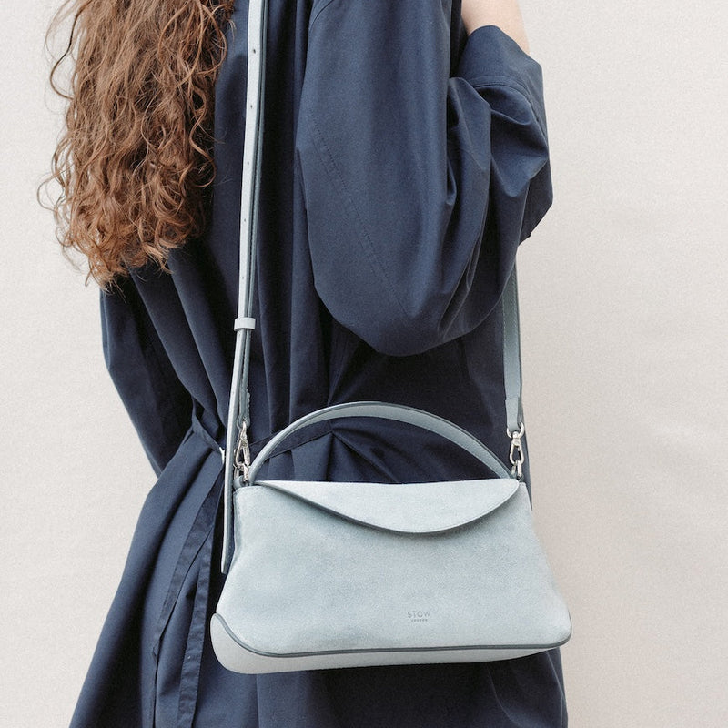 Model wearing STOW London's Mini East West in Misty Blue suede leather on her shoulder featuring silver stainless steel hardware