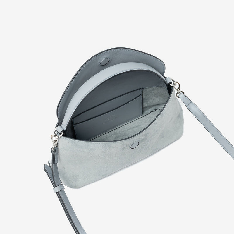 STOW London's Mini East West in Misty Blue suede leather with flap open showing suede interior and slip pocket featuring silver stainless steel hardware on a light grey background