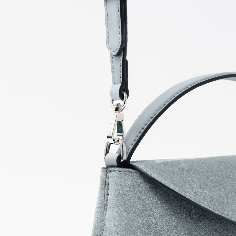 Close up of the detachable crossbody strap clip of STOW London's Mini East West in Misty Blue suede leather featuring gold-coated stainless steel hardware on a light grey background