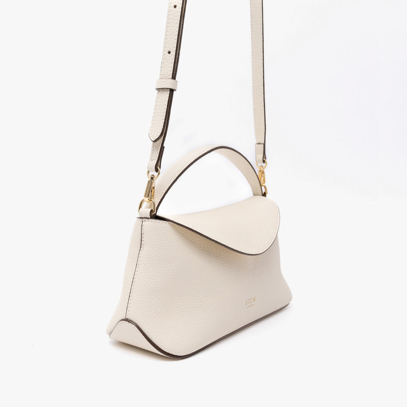 Off-axis view of STOW London's Mini East West in Spring Moon pebbled leather and detachable crossbody strap featuring gold-coated stainless steel hardware on a light grey background