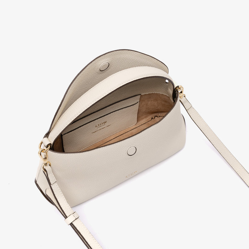 STOW London's Mini East West in Spring Moon pebbled leather with strap open showing suede interior and slip pocket featuring gold-coated stainless steel hardware on a light grey background