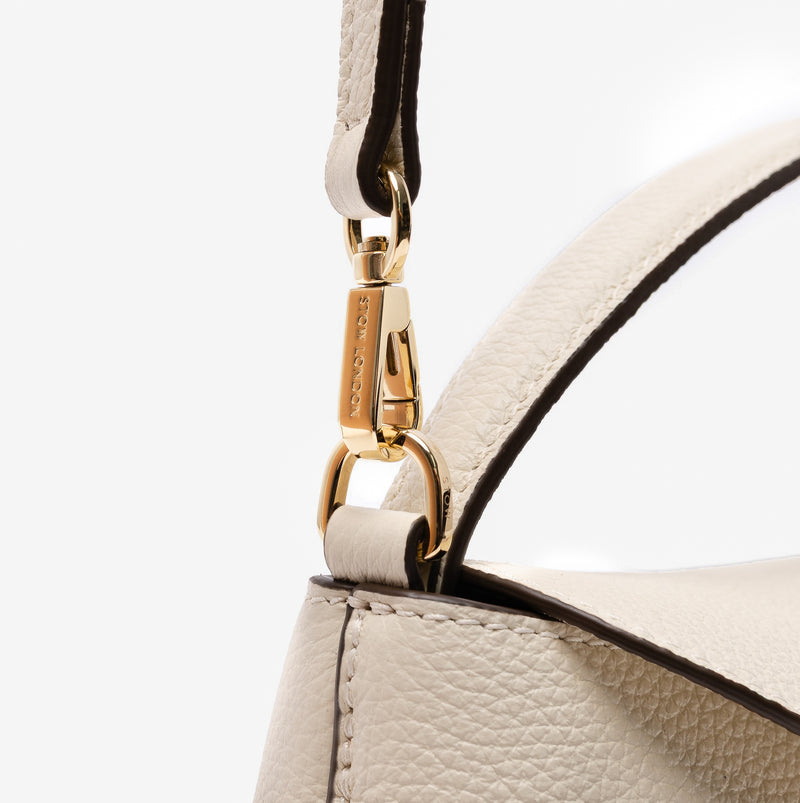 Close up of the detachable crossbody strap clip of STOW London's Mini East West in Spring Moon pebbled leather featuring gold-coated stainless steel hardware on a light grey background